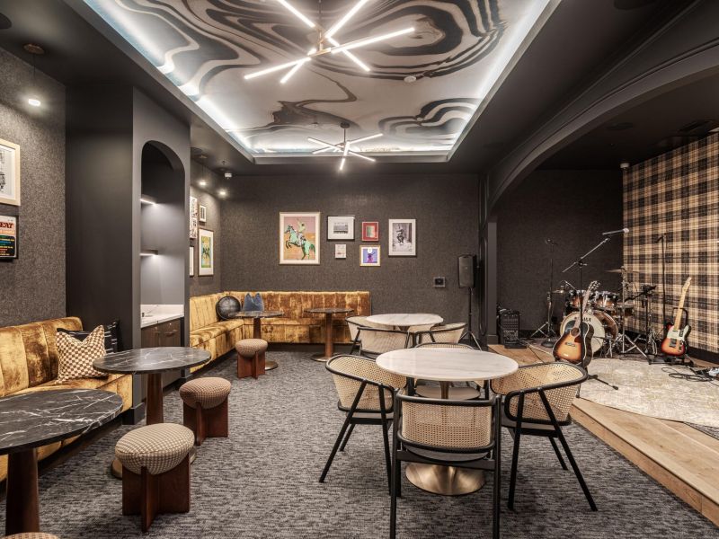 Modern lounge with artistic ceiling, round tables, chairs, sofa, wall art, and a drum set in the corner.