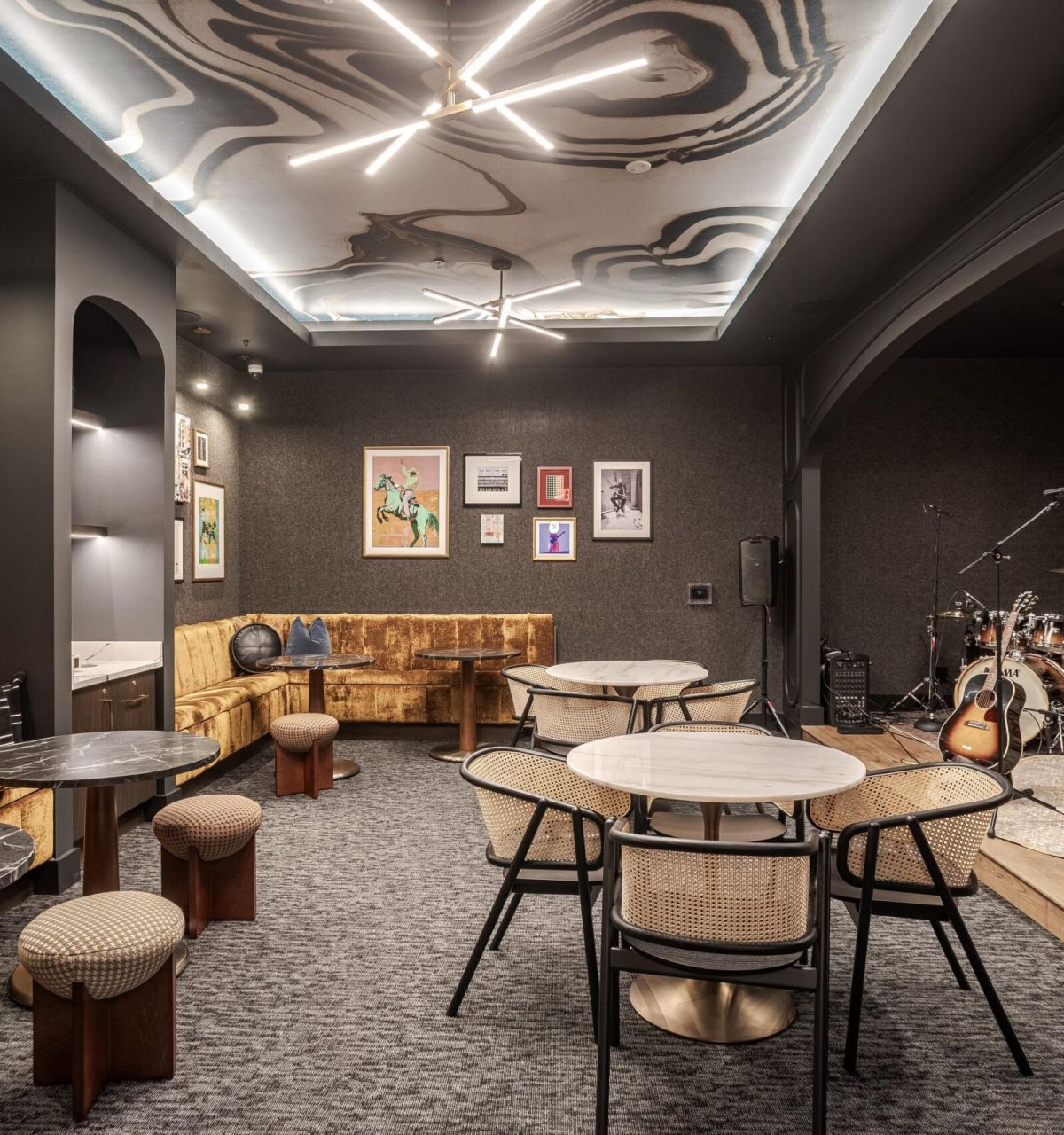 Modern lounge with artistic ceiling, round tables, chairs, sofa, wall art, and a drum set in the corner.