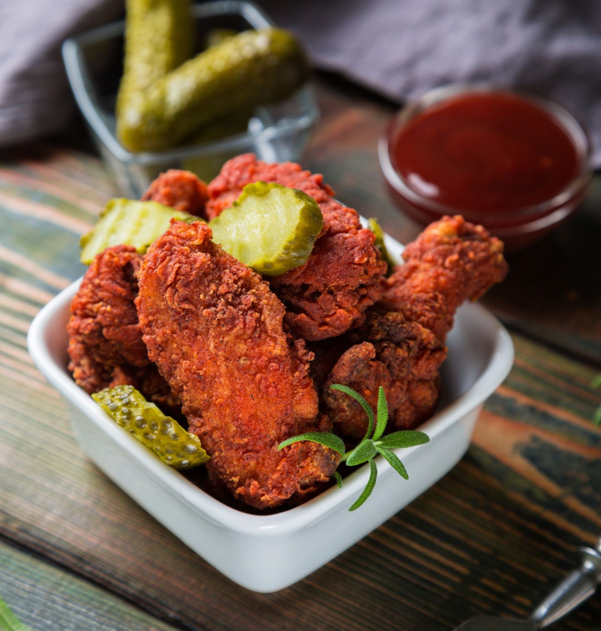 Nashville hot chicken wings and legs in a dish with a side of pickles and bbq sauce