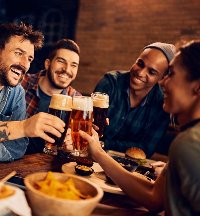 Cheerful man and his friends toast with beer while gathering in bar.