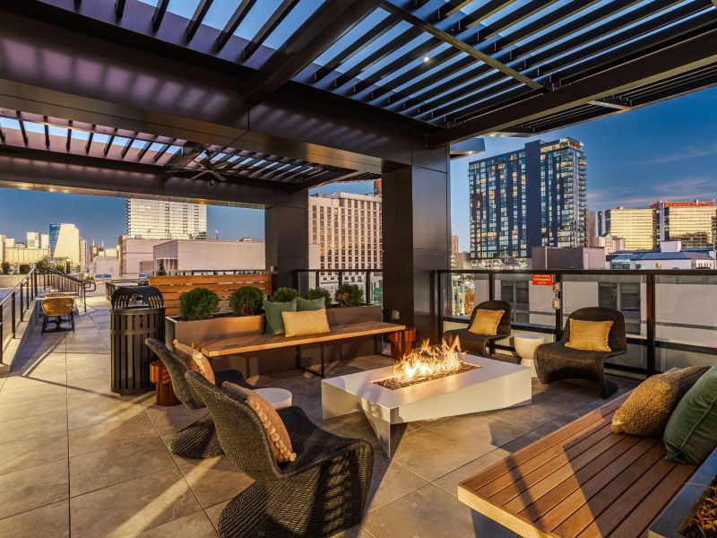 Rooftop terrace with lounge seating and a rectangular fire pit, overlooking a city skyline.